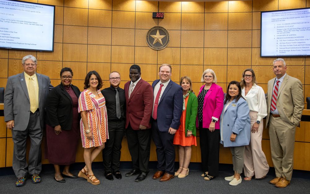 Group of 10 school board members pose together in formal meeting room.