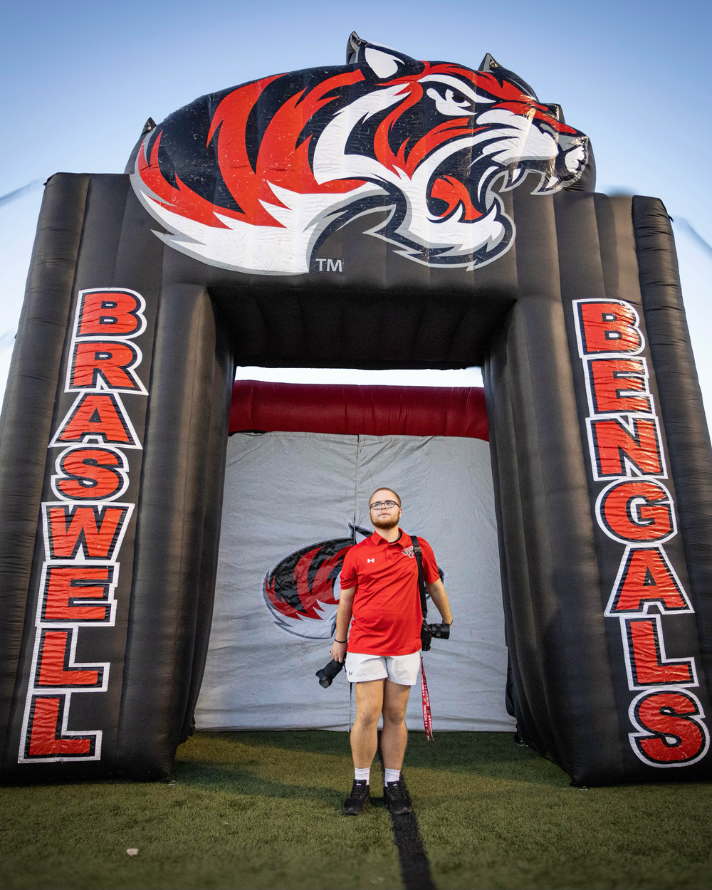 Photographer stands under inflatable Braswell Bengals tunnel mascot arch at football stadium.