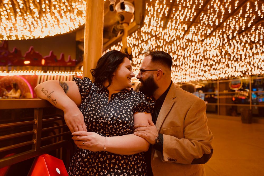 Couple sharing a romantic moment under warm fairy lights at a festive outdoor venue at night.