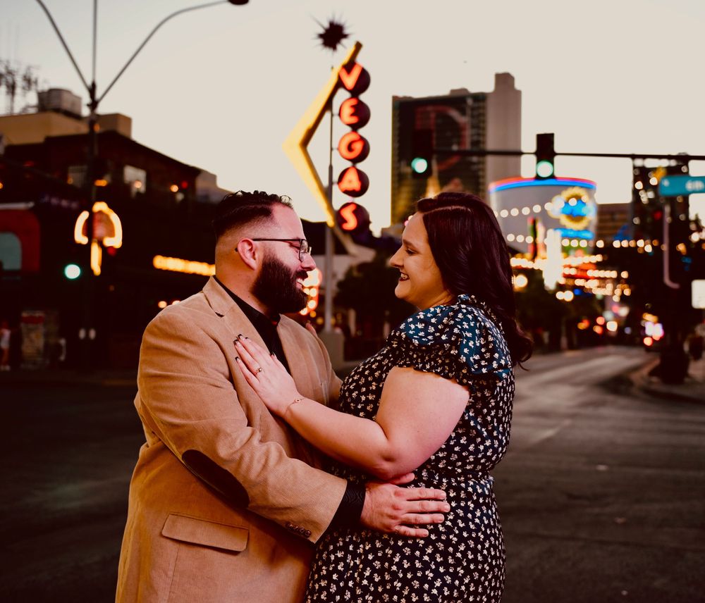 Couple embracing romantically on the Las Vegas Strip at dusk with iconic neon signs glowing in the background.