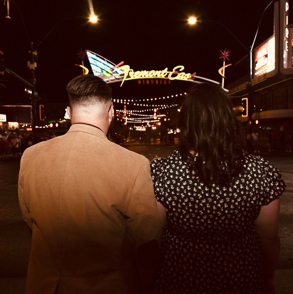 Couple standing together at night facing the iconic Fremont East neon sign in Las Vegas, Nevada.