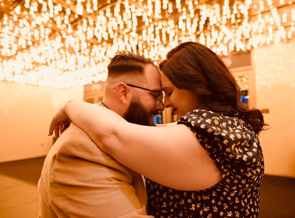 Couple sharing a romantic forehead touch under warm glowing chandelier lights in an elegant indoor venue.