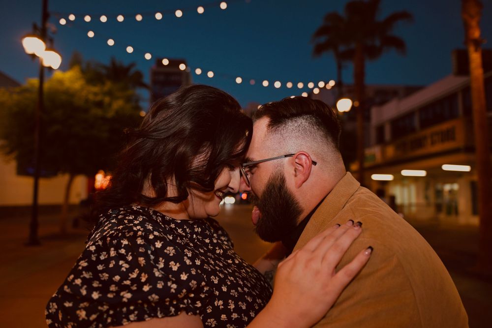 Couple sharing a romantic moment outdoors at night under string lights with palm trees in background.