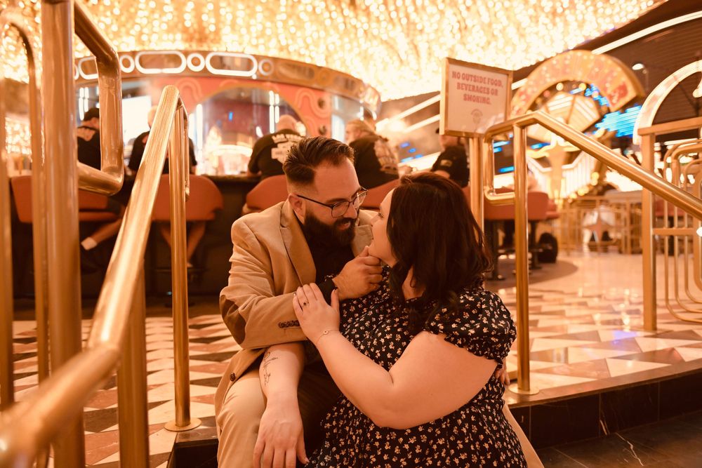 Couple sharing a romantic moment on carousel steps, man in tan blazer holding woman's hands in floral dress.