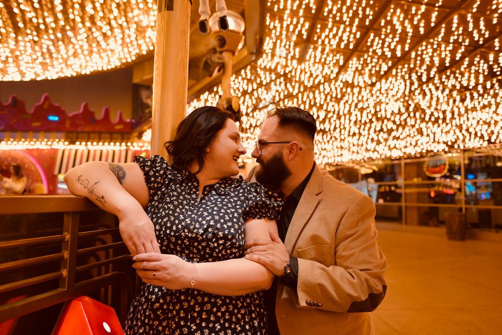 Couple sharing a romantic moment under warm string lights at a festive outdoor venue at night.