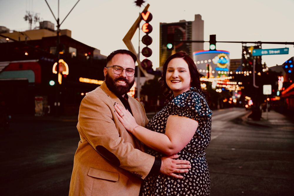 Couple embracing and smiling on a vibrant city street at sunset with colorful neon signs in the background.