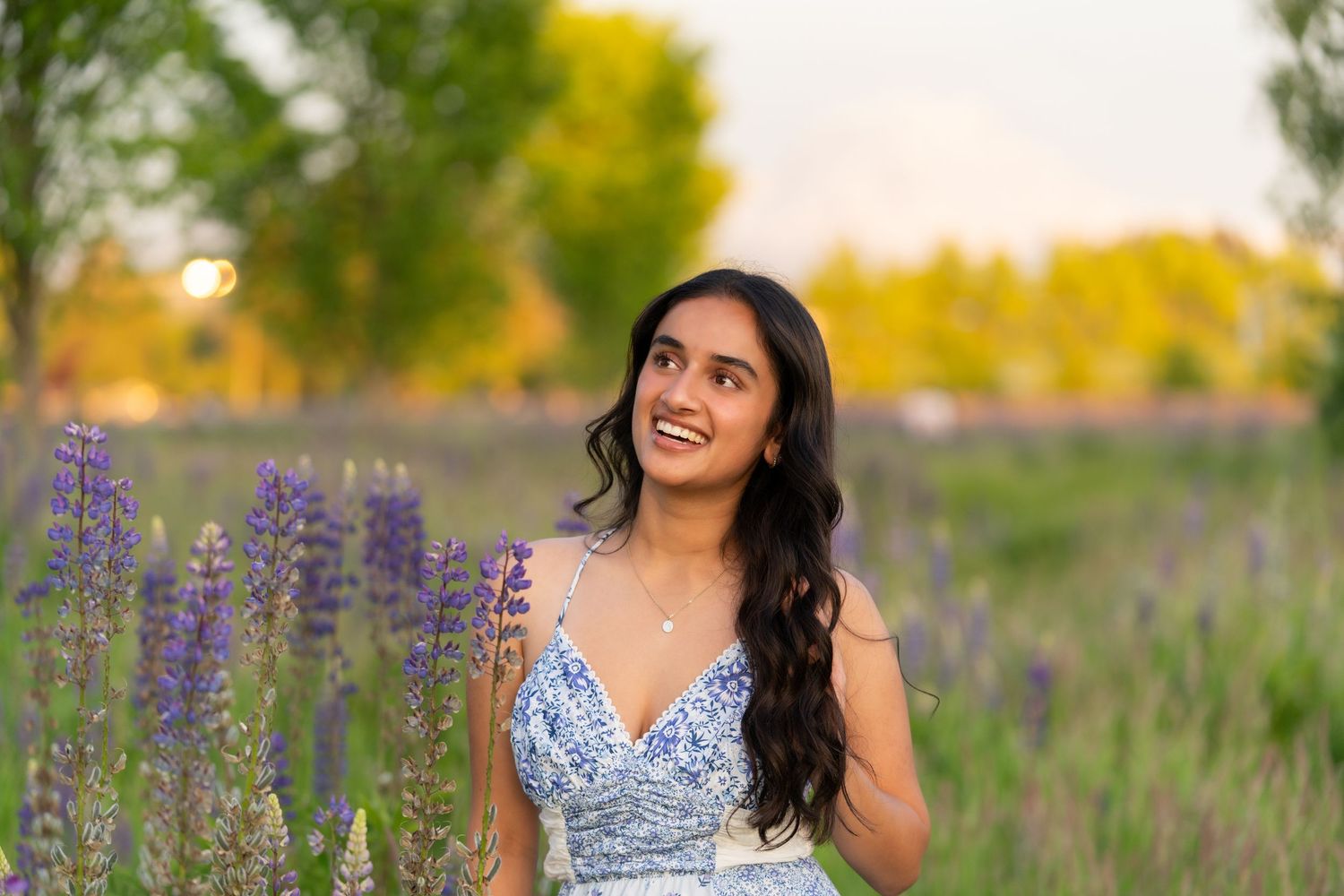 Young woman in floral dress smiling in a lavender field at golden hour sunset.