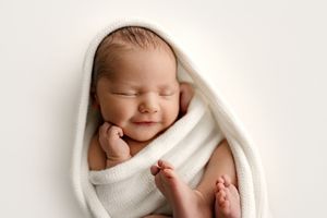 Smiling newborn baby wrapped in soft white blanket, peaceful sleeping pose, professional newborn photography.