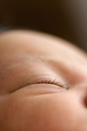 Close-up macro photo of a sleeping newborn baby's closed eye with delicate eyelashes on soft skin.