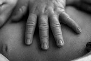 Close-up black and white photo of a hand resting on a bare stomach, showing detailed skin texture and nails.