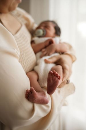A mother holds her newborn baby, showcasing the infant's tiny feet in soft focus while feeding with a bottle.