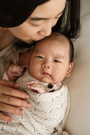 A mother tenderly kisses her newborn baby wrapped in a cozy knit blanket, sharing a peaceful bonding moment.