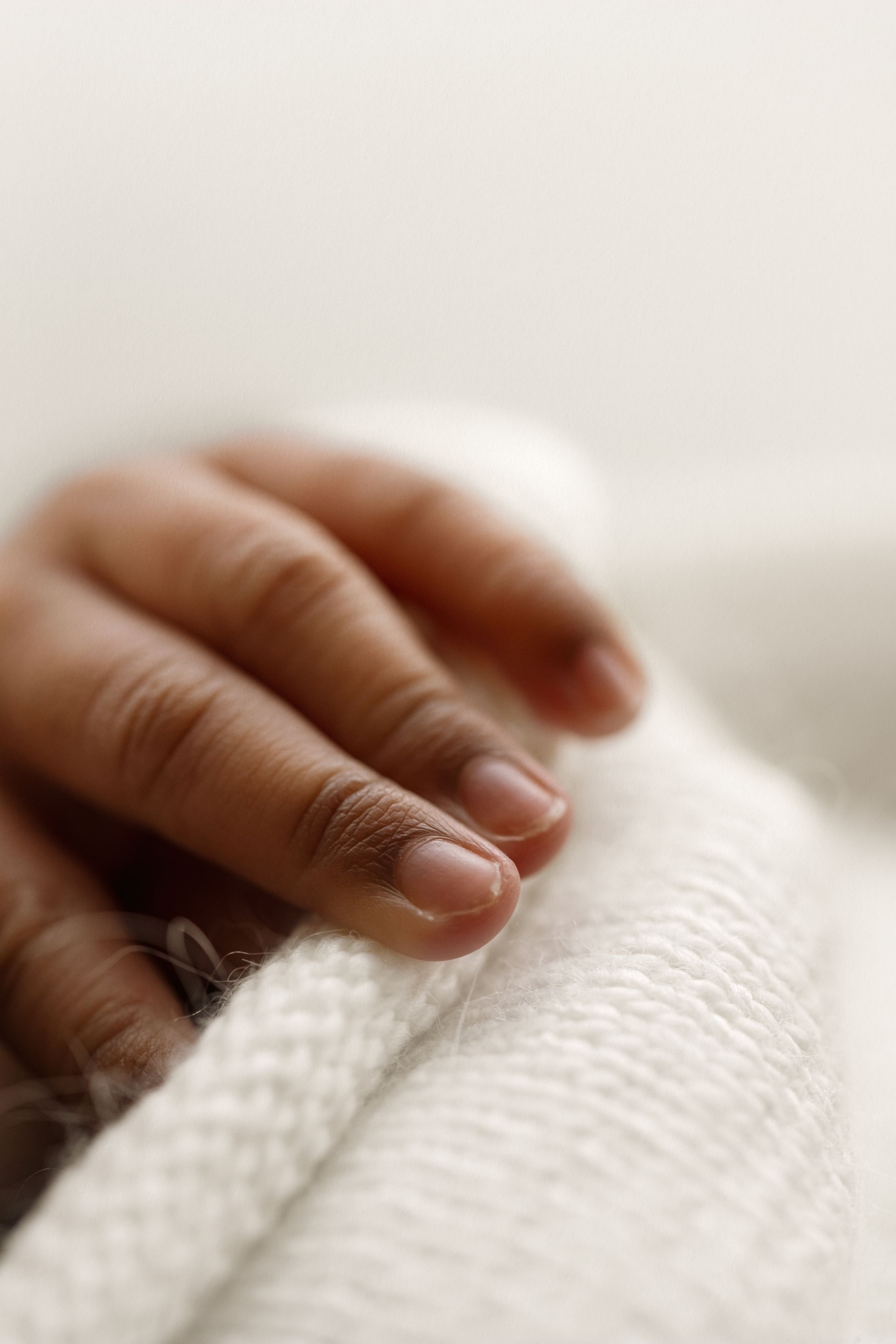 Close-up of a newborn baby's tiny hand resting gently on a soft white knit blanket.