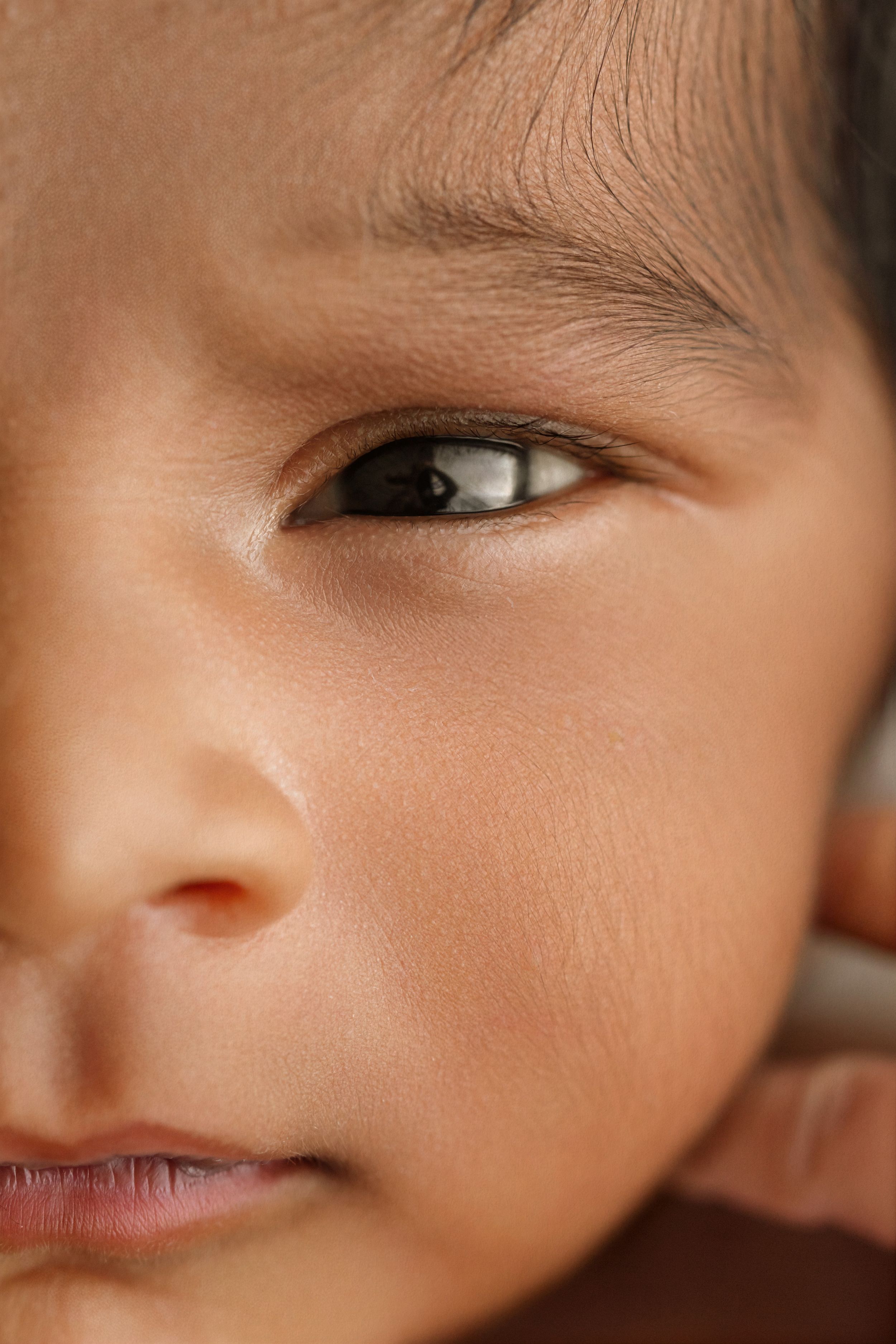 Close-up portrait of a newborn baby's face with dark eyes and smooth skin.