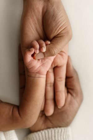 A newborn baby's tiny hand gently grasping an adult's finger, symbolizing love and new parenthood.