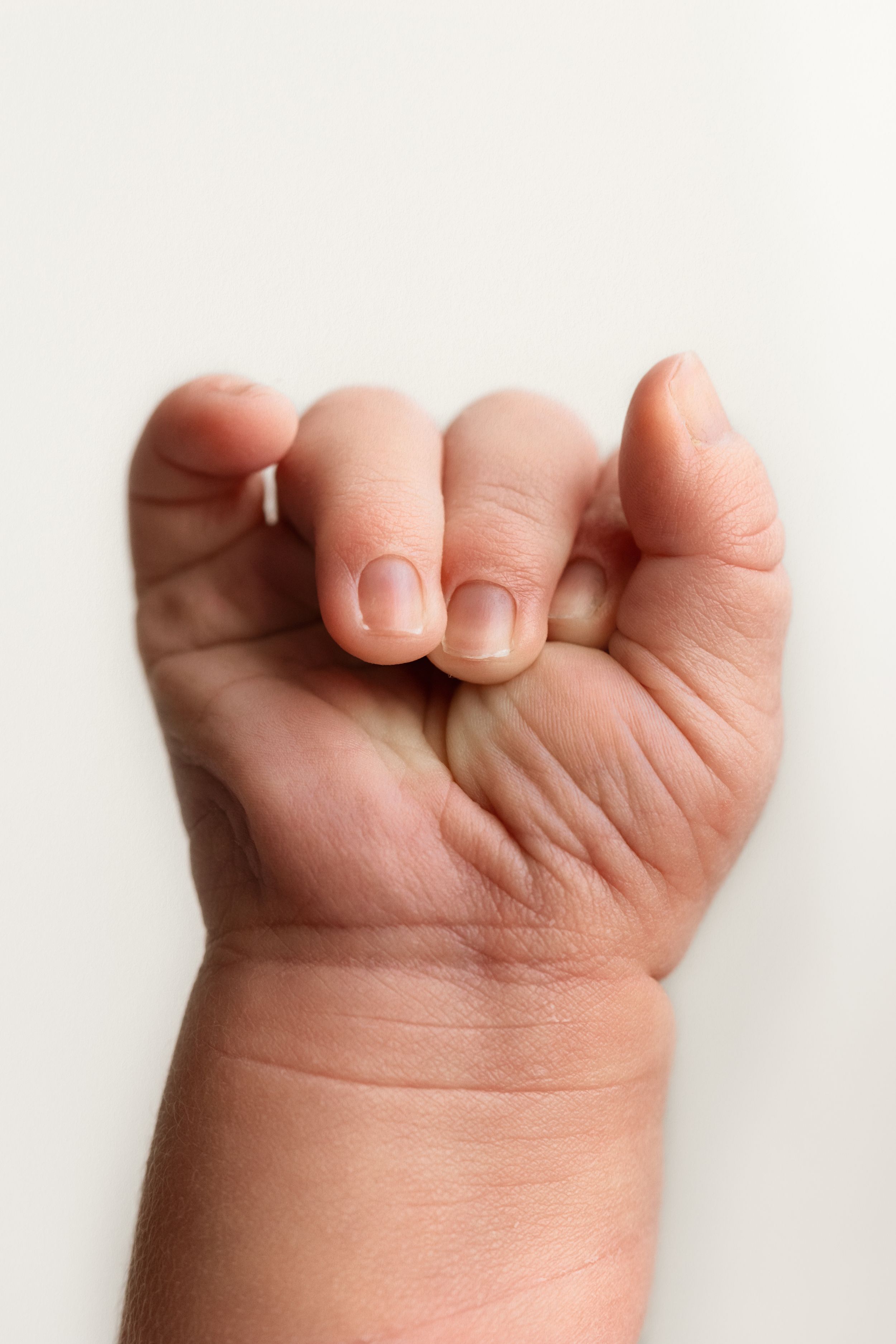 Close-up of a newborn baby's tiny clenched fist against a white background.