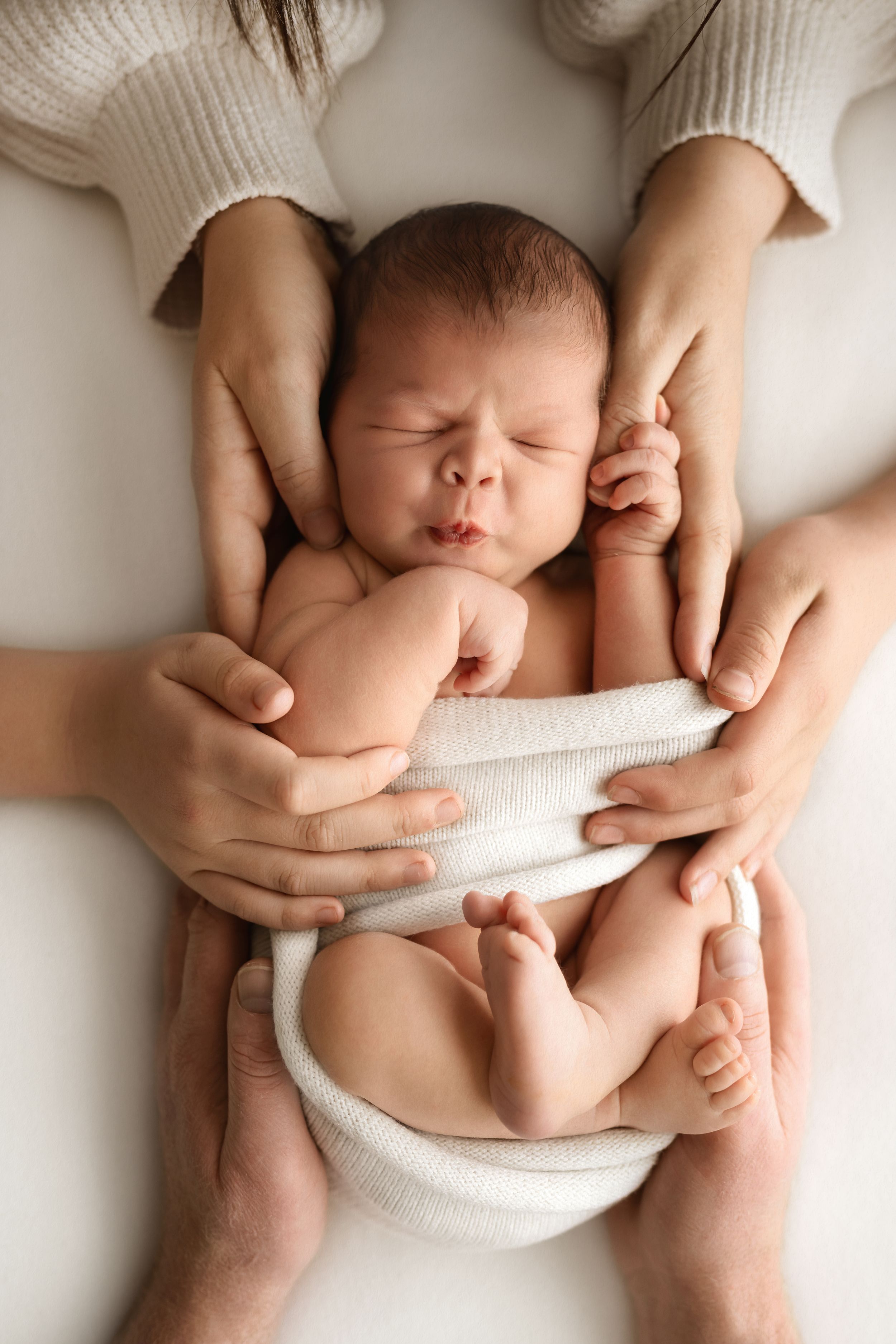 Newborn baby sleeping peacefully cradled in parents hands on white background.