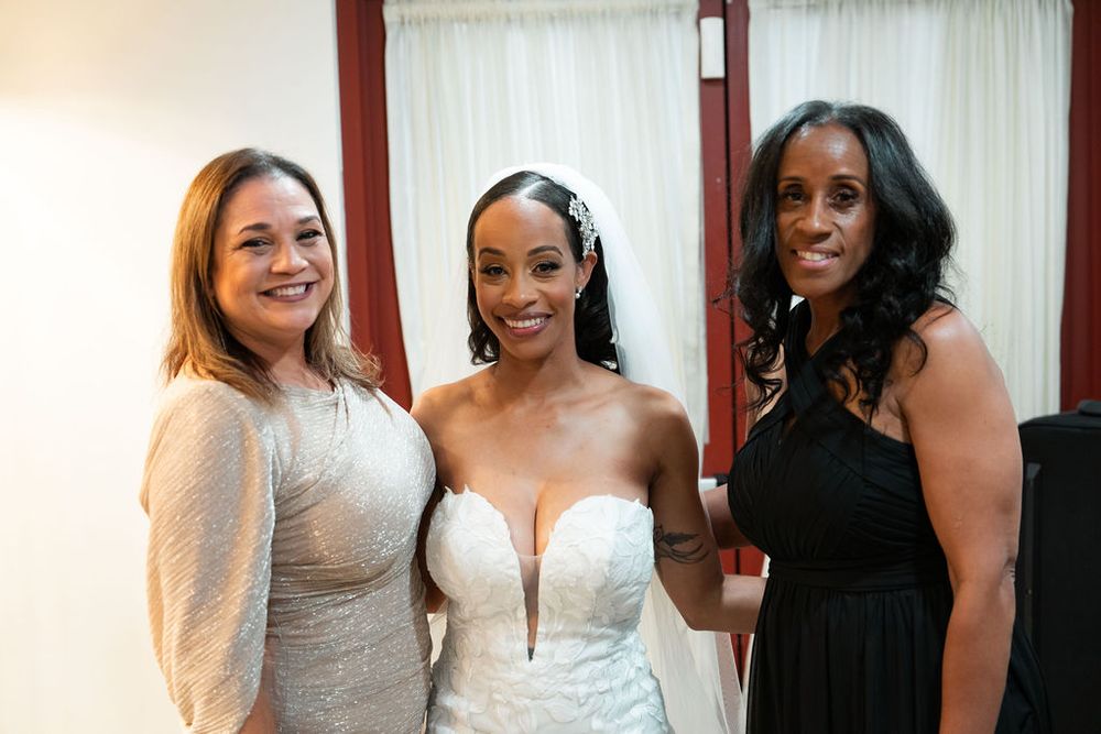 Bride in white gown poses with two women in formal attire at a wedding celebration.