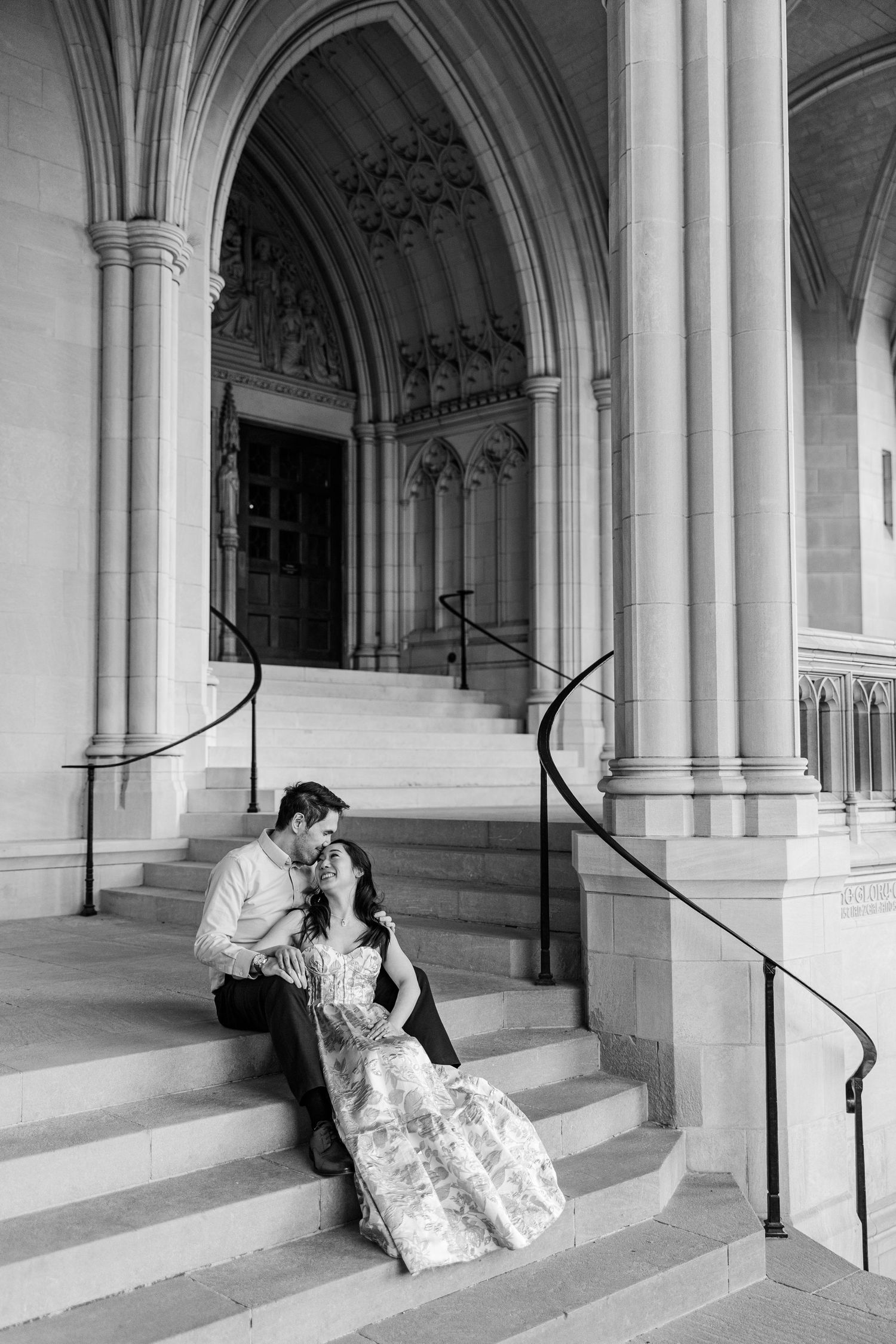 Black and white photo of a couple sharing a romantic moment on cathedral steps, bride in floral gown.