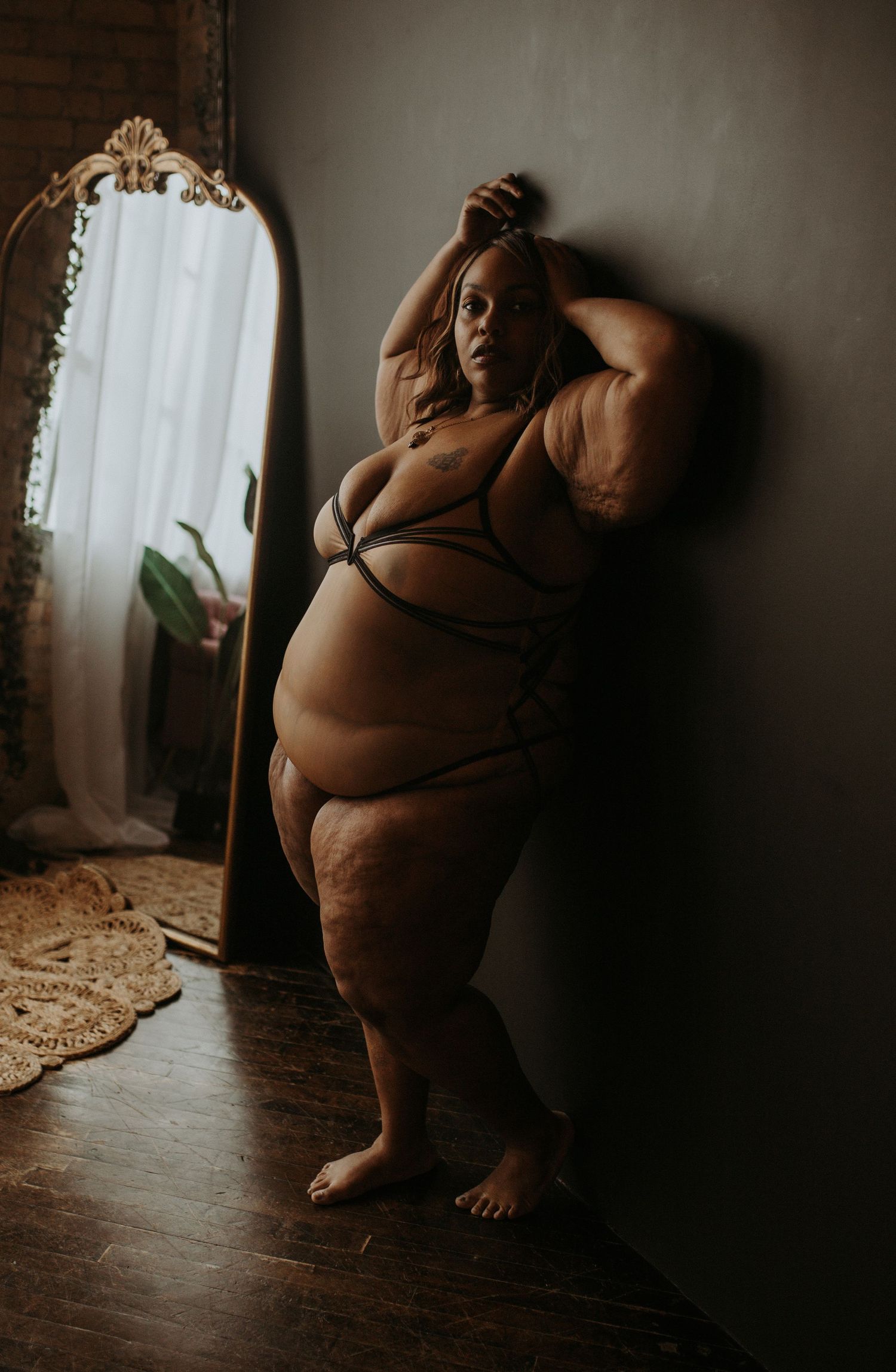 Woman in white lingerie posing on a wooden stool near a vintage mirror in warm natural light.
