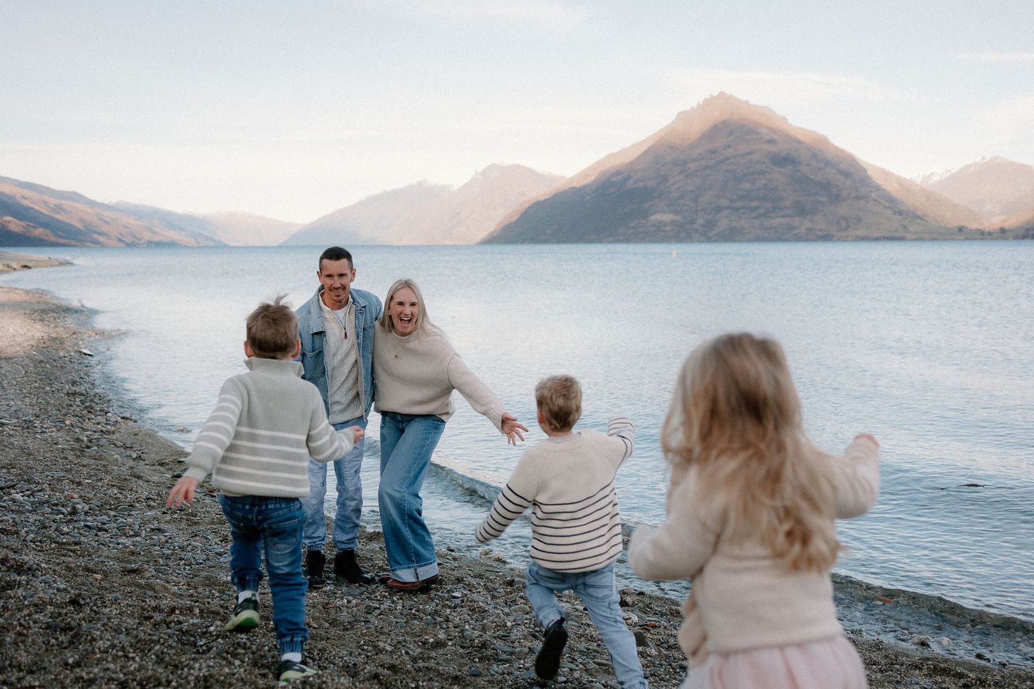 Family with two young children running through golden fields with snow-capped mountains in the background.