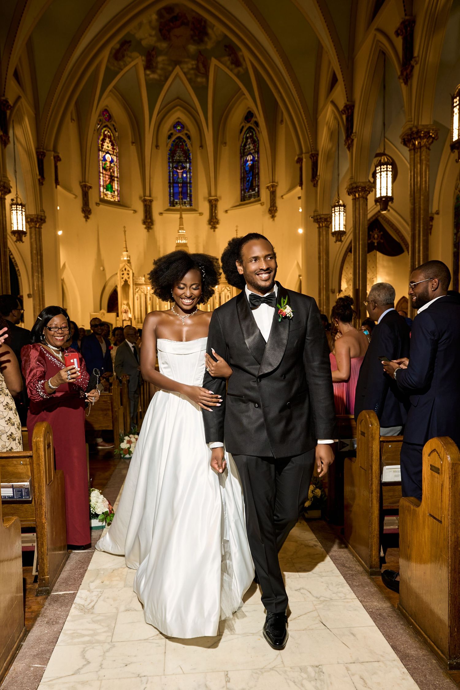 Newlywed couple walks down church aisle after wedding ceremony, bride in white gown and groom in black tuxedo.