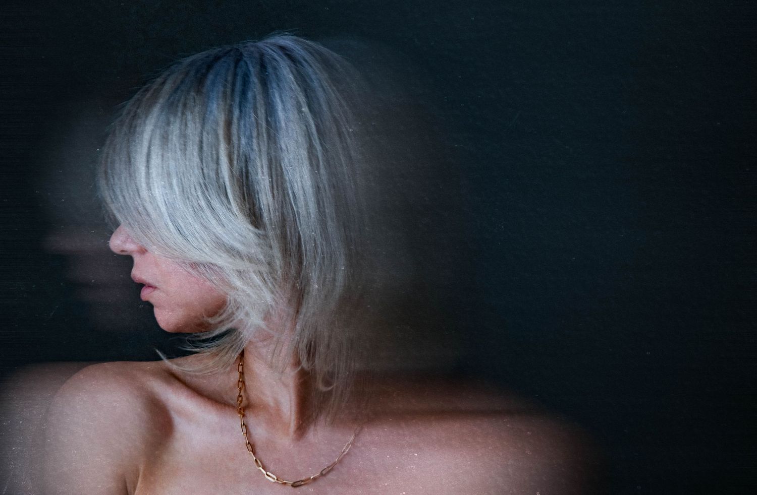 Woman with silver-gray bob haircut posing against dark background, hair sweeping across face.