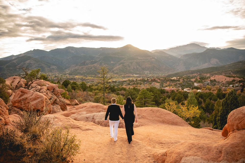 Couple holding hands walking on red rock trail with stunning mountain sunset views in Colorado.