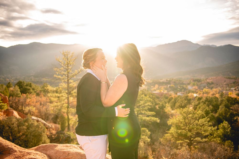 Couple embracing on rocky overlook with golden sunset light and mountain valley view.