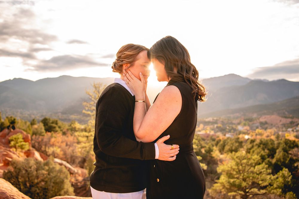 Two women sharing a romantic moment at sunset with mountain landscape backdrop.