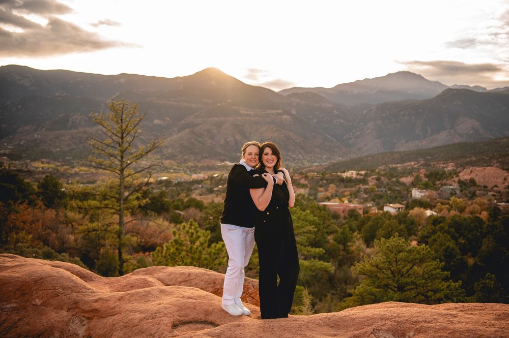 Two women embrace on red rocks at sunset with mountain views at Garden of the Gods, Colorado.