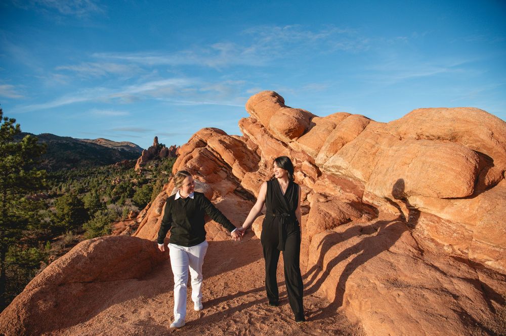 Two people stand atop red rock formations at Garden of the Gods, Colorado, under a clear blue sky.