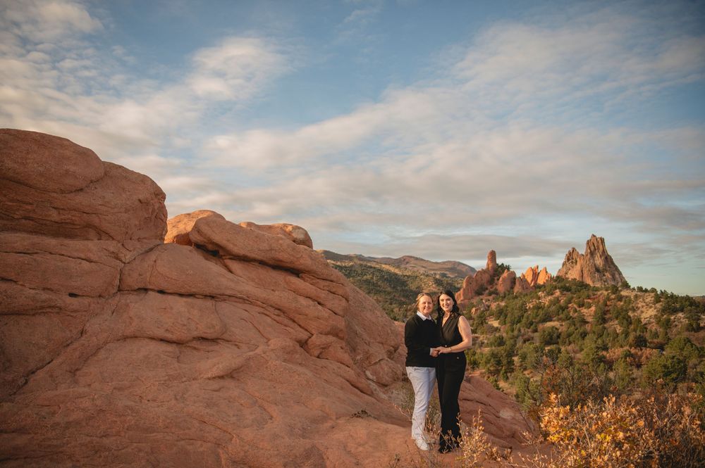 Couple embracing at Garden of the Gods with red rock formations and dramatic Colorado landscape at sunset.
