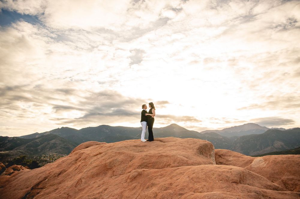 Couple embracing on red rocks at sunset with mountain backdrop at Garden of the Gods, Colorado.