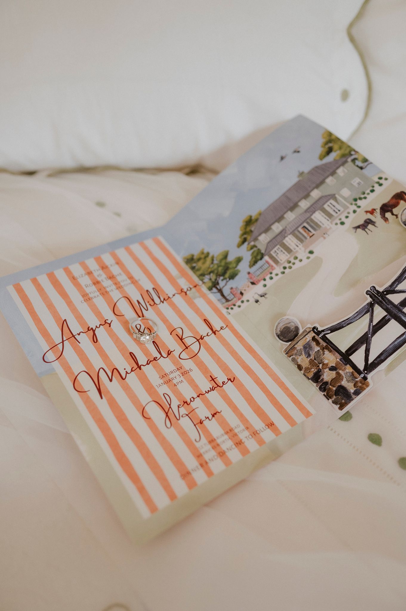 Wedding invitation suite with orange striped card and illustrated venue watercolor on white bedding.