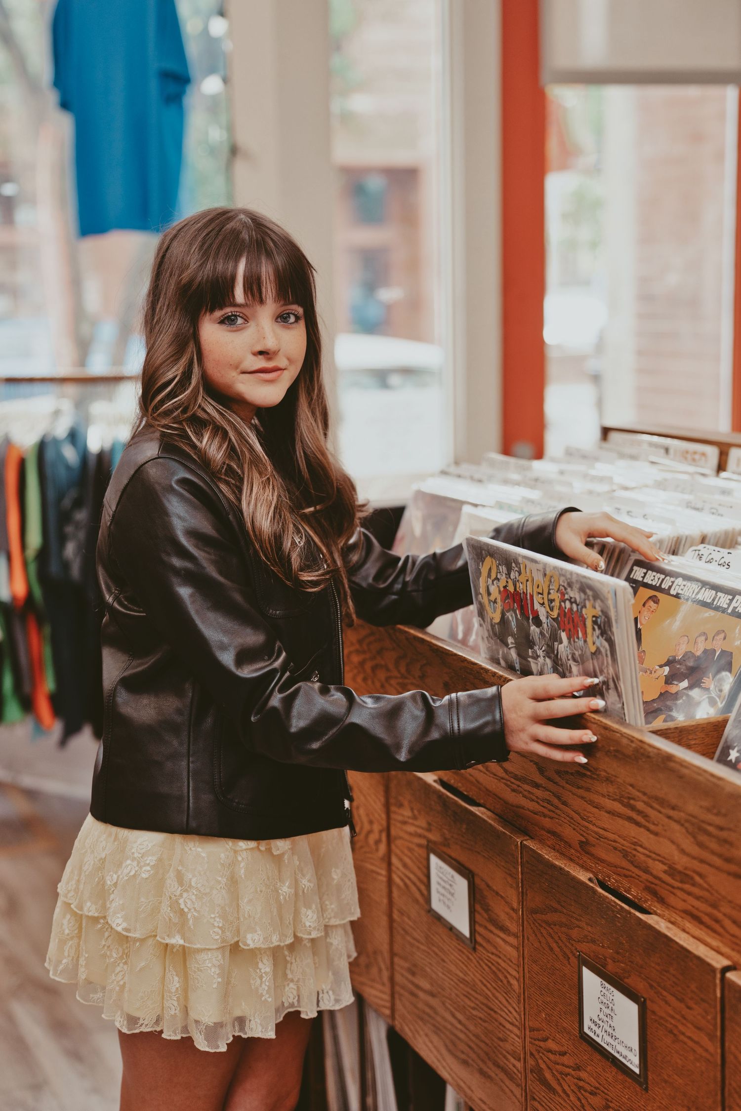 Young woman in red top and black jeans browsing vinyl records in a cozy music store.
