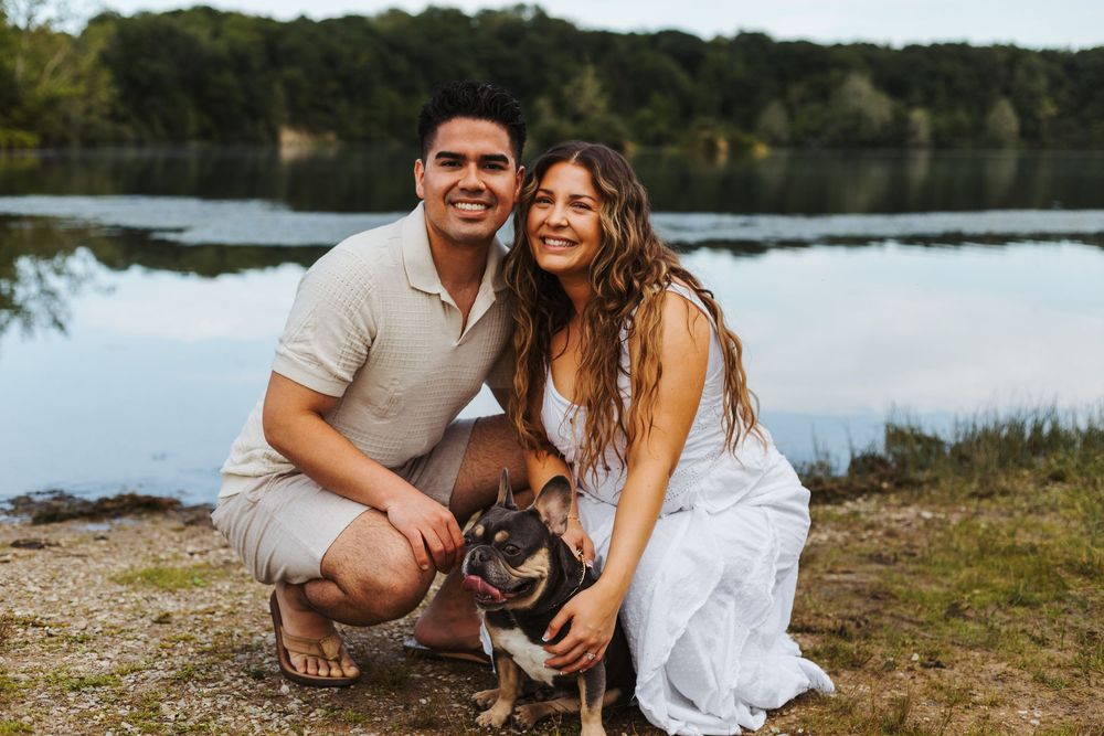 Couple smiling with their dog by a Eagle Creek Park surrounded by lush green trees.
