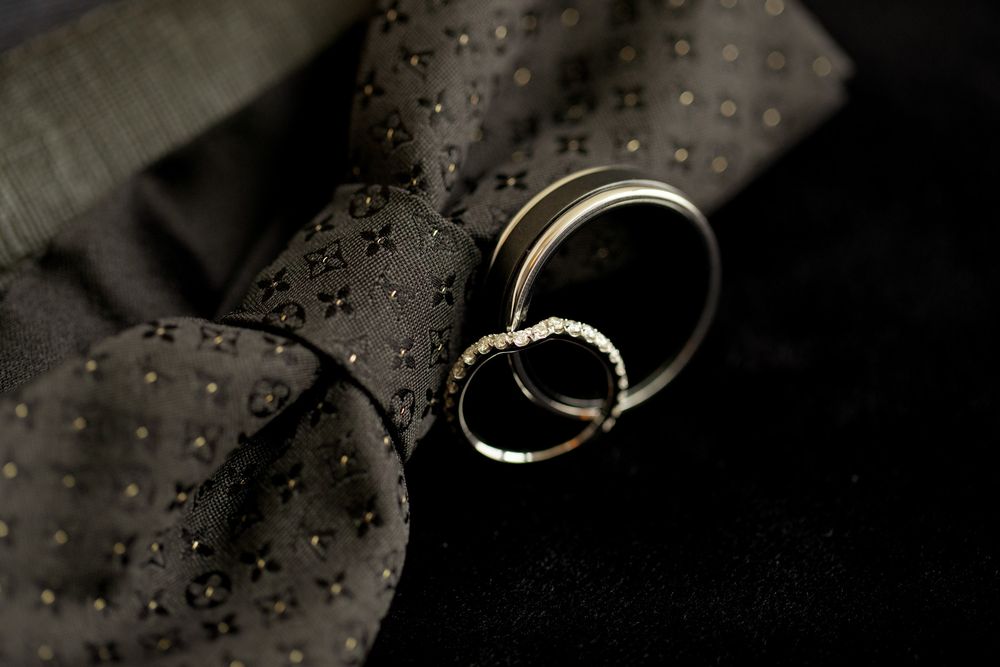 Two gold wedding rings resting on a dark patterned tie, symbolizing marriage and elegance.