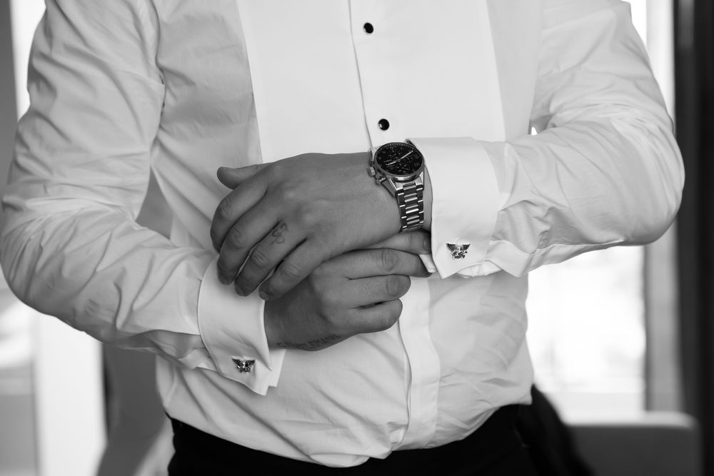 Black and white photo of a man in a white dress shirt adjusting his cufflinks while wearing an elegant watch.
