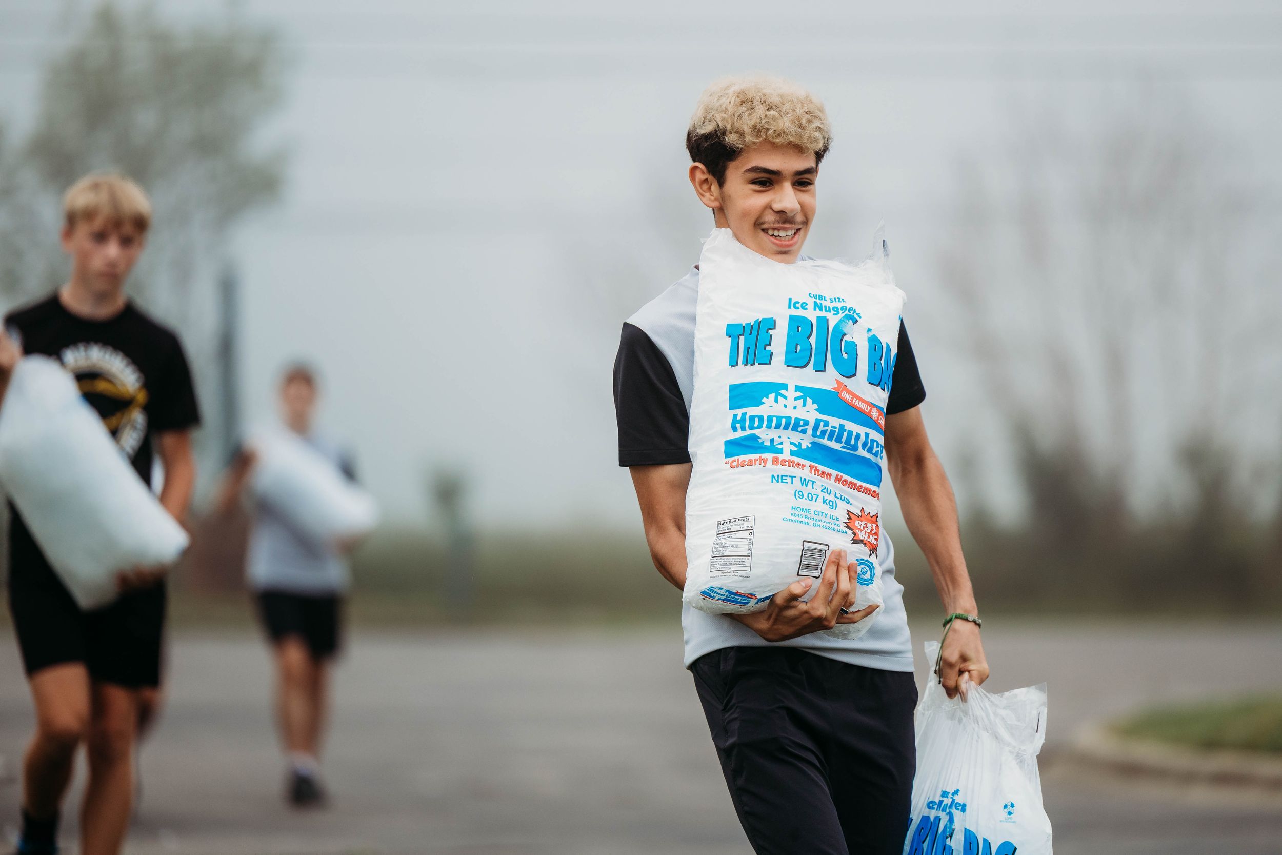 Smiling teen carrying bags at The Big Event community service project outdoors.