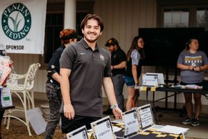 Man in polo shirt smiling at outdoor sponsor event table with Penline Seeding sign in background.