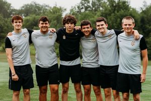 Six young male soccer players in gray uniforms pose together smiling on a green field.