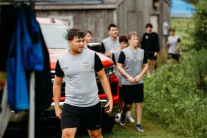 Young male soccer players in athletic wear gather outdoors near a barn during a team training session.