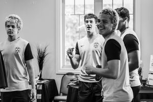 Group of young men in matching soccer jerseys laughing and socializing indoors in black and white photo.