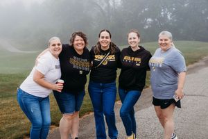 Five women smiling together outdoors on a foggy day, wearing college spirit wear and casual clothing.