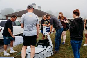 Group of people assembling outdoor equipment on a foggy day near a white house and parked truck.