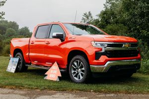 Bright orange Chevrolet Silverado pickup truck displayed outdoors on green grass at an automotive event.