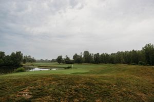 Lush green golf course fairway with a pond, trees, and overcast sky in a serene outdoor landscape.