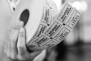 A hand holding a large roll of raffle tickets with perforated stubs in black and white photography.