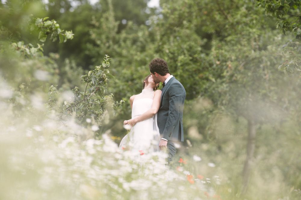 A bride and groom share a romantic kiss surrounded by wildflowers and lush greenery on their wedding day.